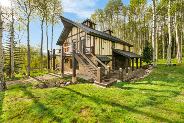 Rustic two-story cabin with a stone foundation and wooden deck in a forest of aspen trees