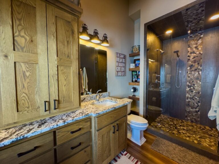 Bathroom with natural wood cabinets, granite countertop, and a single sink mirror setup beside a glass-enclosed shower area.