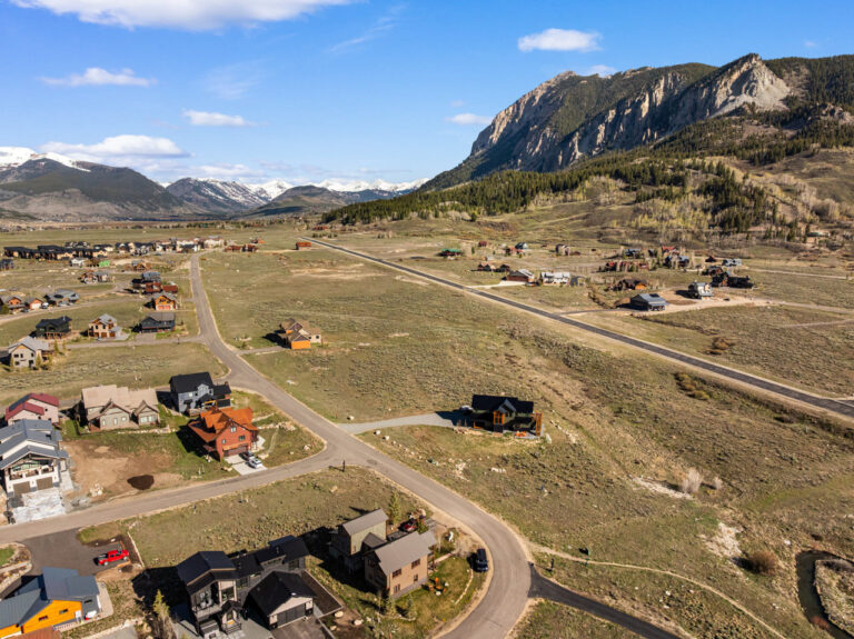 Aerial view of a mountain valley village with winding roads and scattered houses under a blue sky. (informational photo) 10-20 words ideal for context navigation only the alt text should suffice as a summary of the scene.