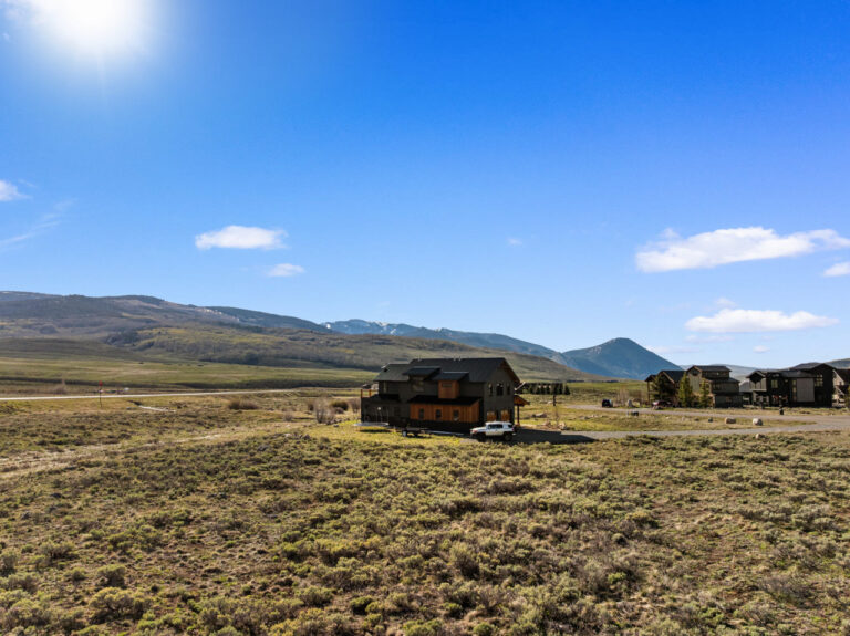 Sunny blue sky over a rural landscape with a modern wooden house and distant mountains under bright sunlight