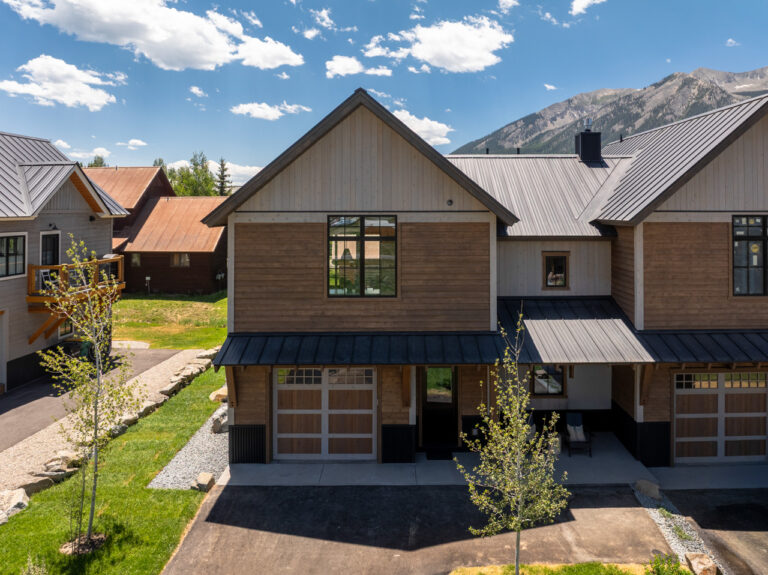Row of modern wooden townhouses with metal roofs against a blue sky and distant mountains.